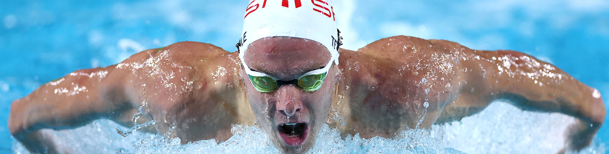 Matt Temple with a swimming cap and goggles on emerging from the water