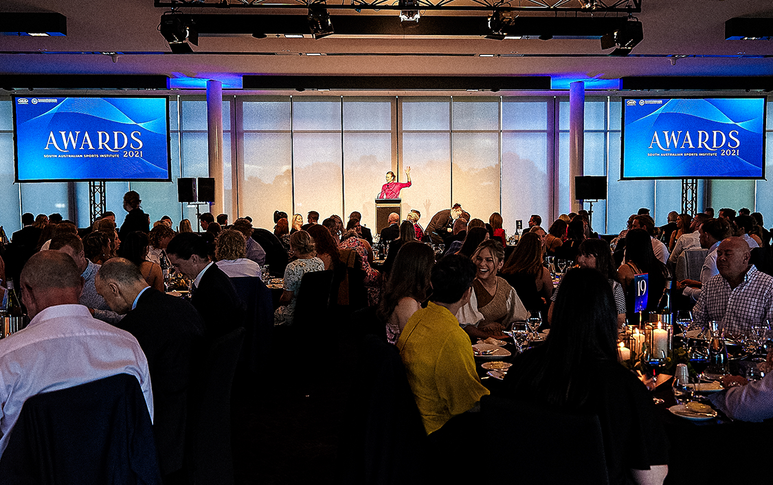 A room full of people sitting down at tables looking at the presenter on stage