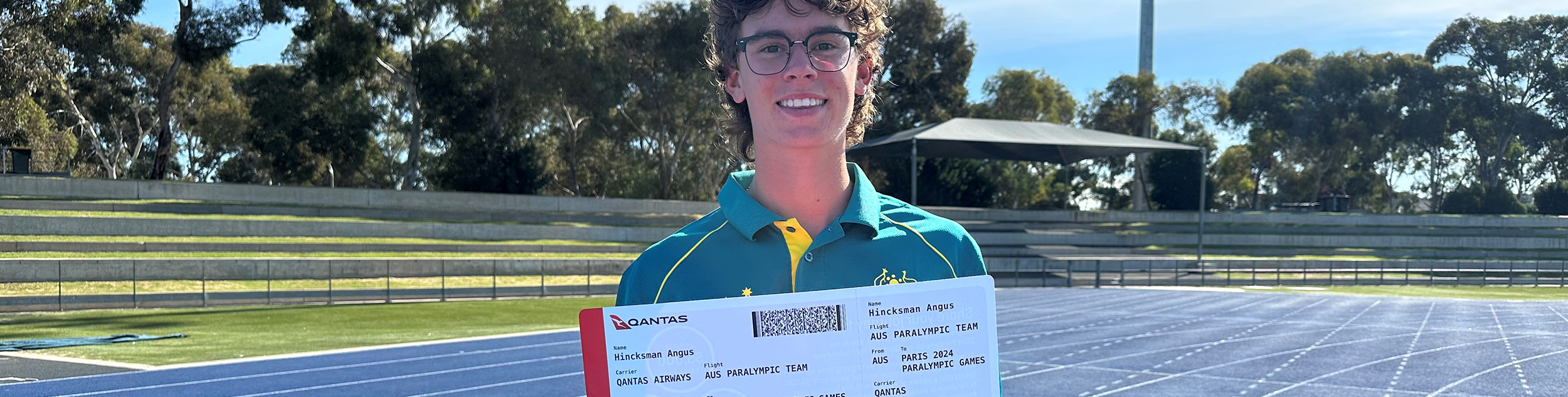 Angus Hincksman stands on an athletics track holding his ticket to the Paris Paralympic Games