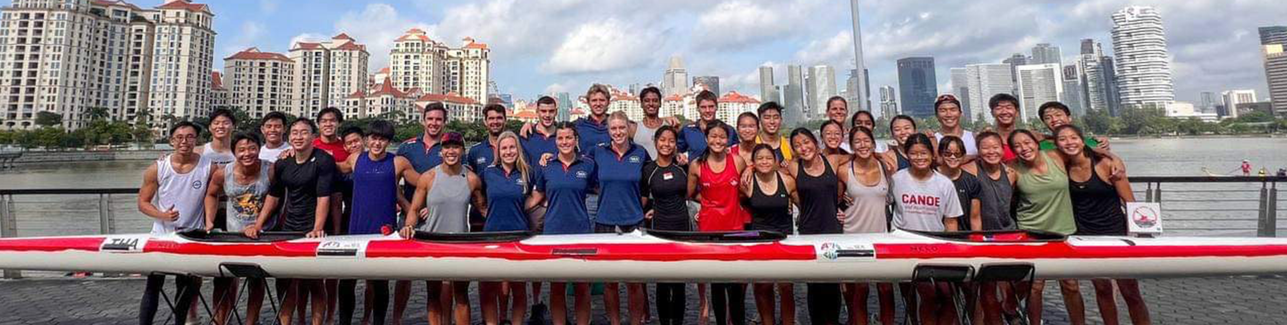 Athletes standing behind a boat with water and buildings in the background
